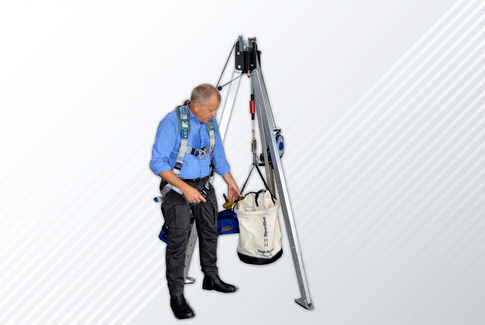 A worker using an industrial lifting tripod to lift a bag safely on a job site.